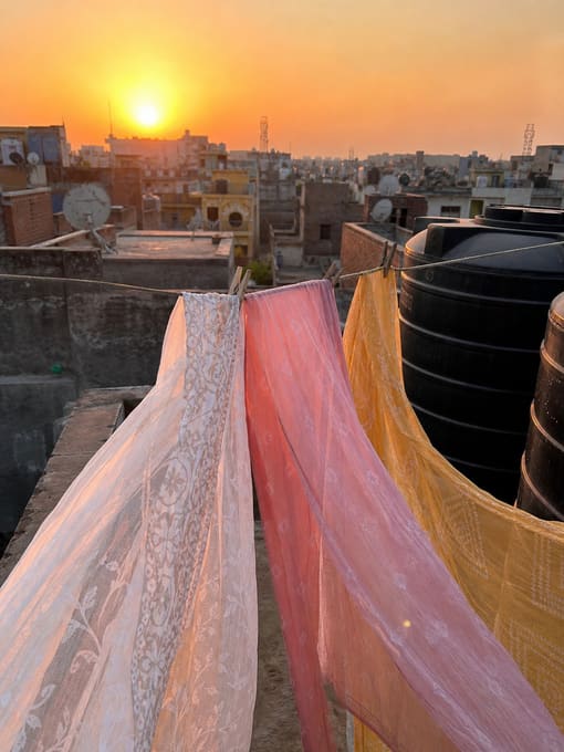 Dupattas drying on a rooftop line against a city sunset